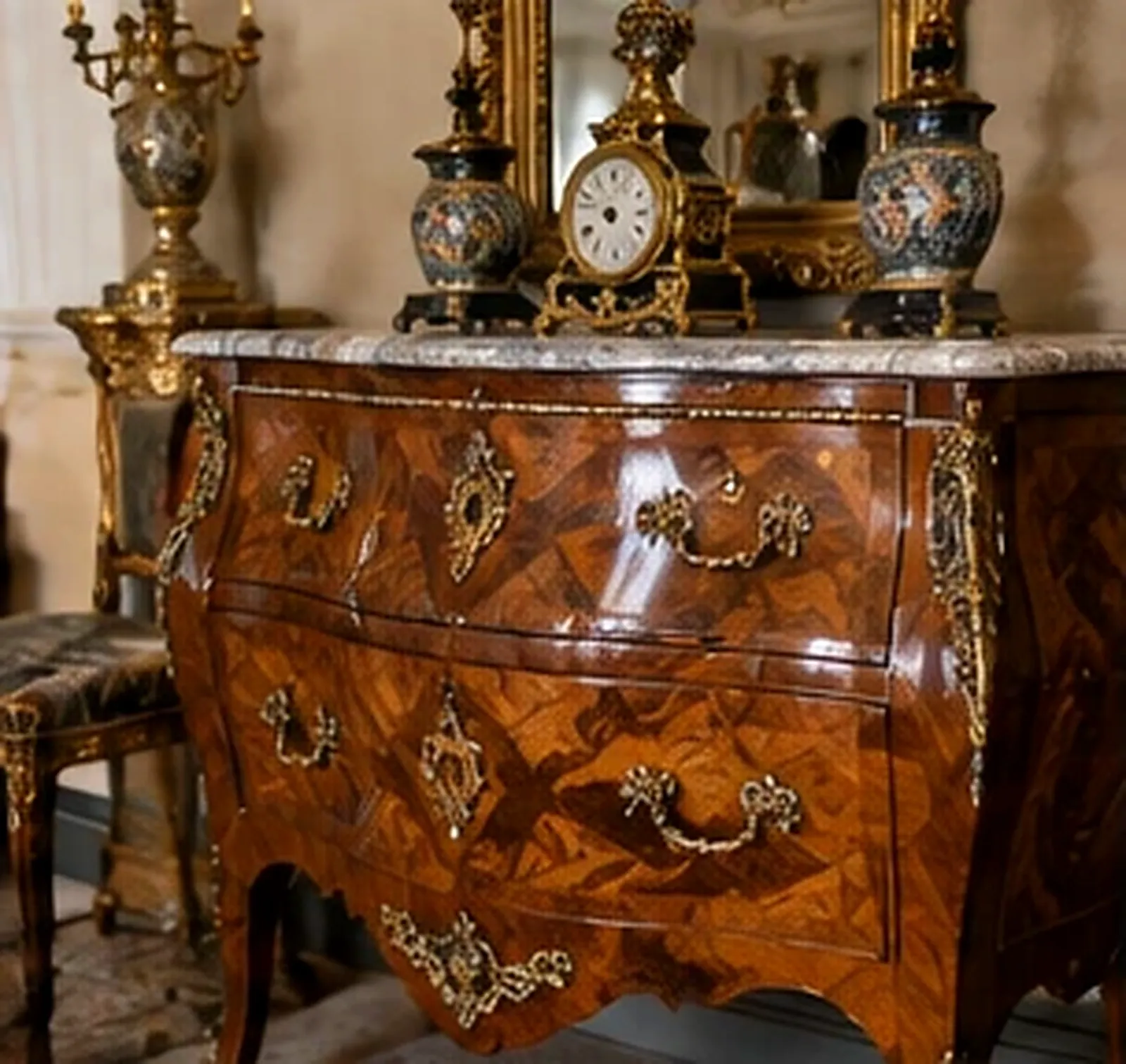 Commode ancienne galbée en marqueterie de bois avec poignées en bronze doré et plateau en marbre, surmontée d'une pendule, de vases et d'un miroir doré